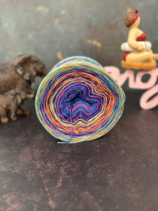 Zu sehen ist ein bunter Bobbel mit blauen, pinken, orangen und grünen Farben auf einem grauen Hintergrund und Dekoration.